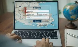 Laptop displaying a booking form with destination, check-in and check-out dates, and guests fields. Background shows a map of Louisiana