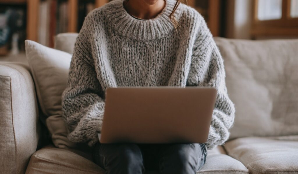 Person sitting on a couch in a sweater using a laptop at home